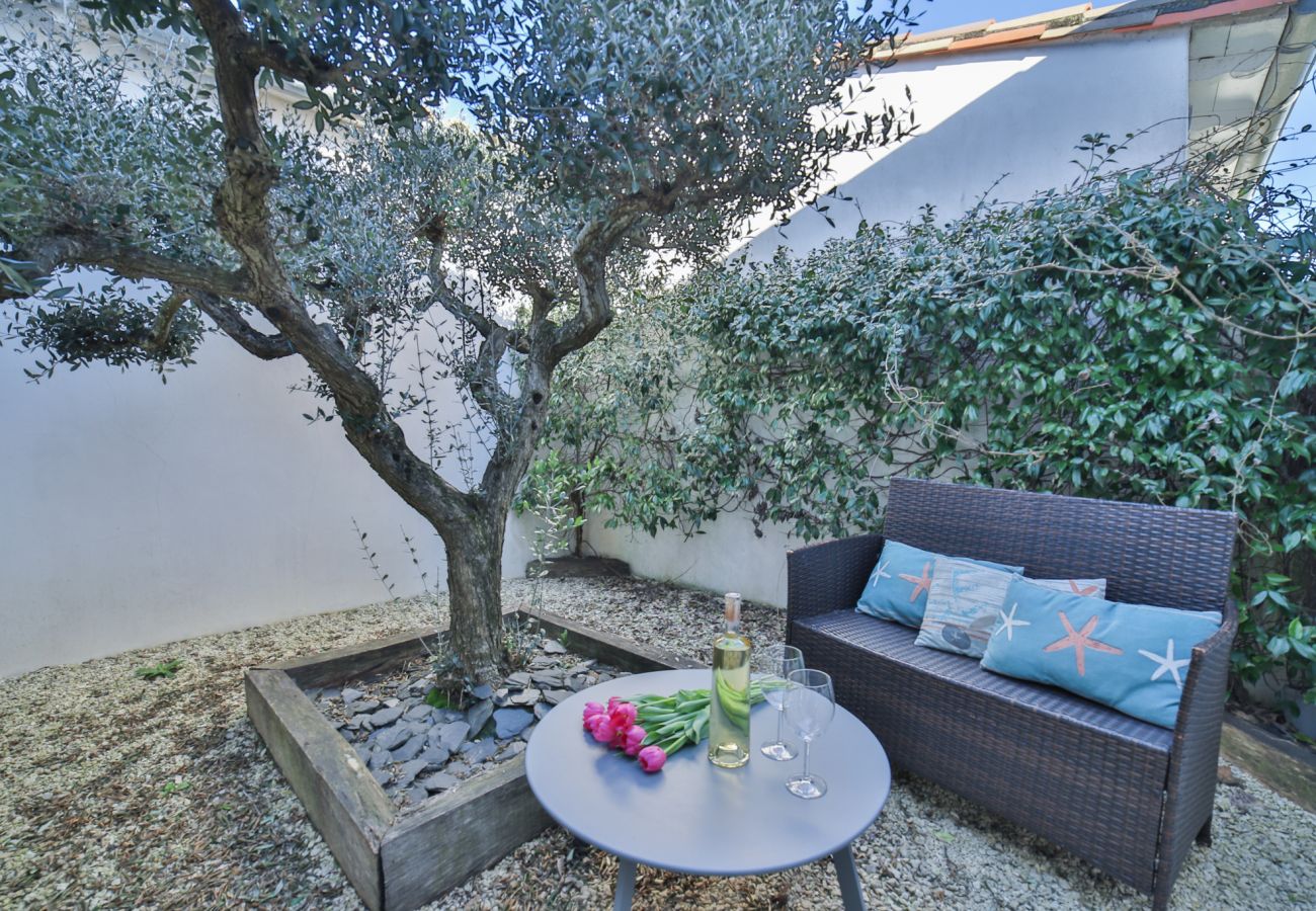 A corner of the garden with a sofa and a table under an olive tree 