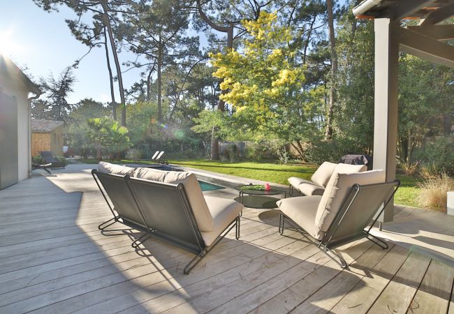 Wooden terrace with armchairs and view of the pool and wooded garden