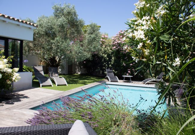 View of the pool with wooden decking, sun loungers and lush garden